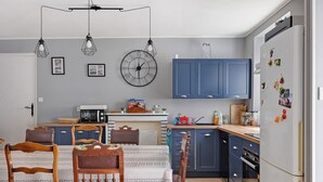 Eine moderne Küche mit blauen Schränken, einem Esstisch mit Stühlen, einer Uhr und einem Kühlschrank mit Magneten.