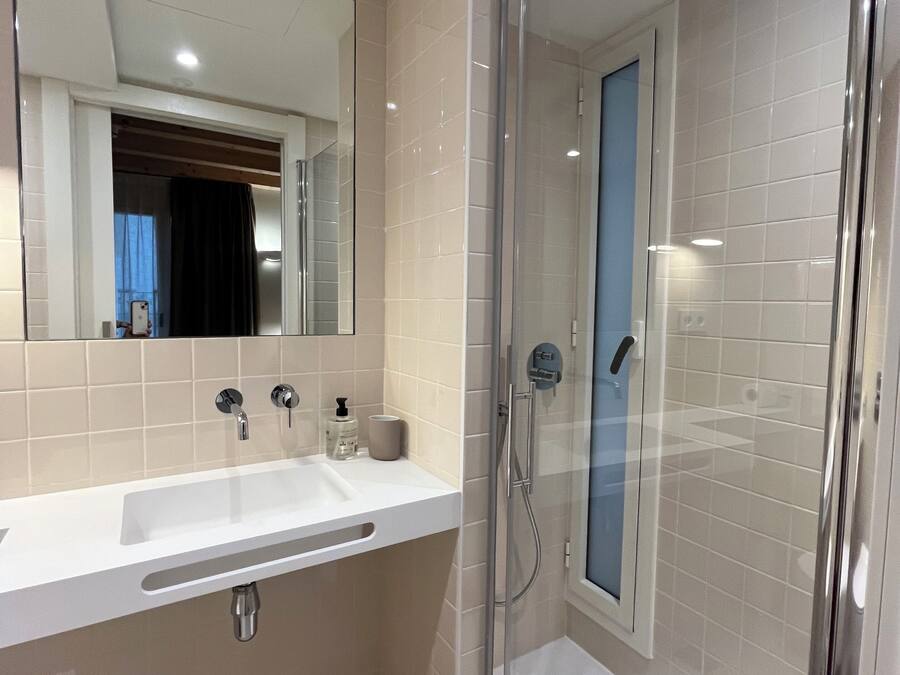 A modern bathroom with a glass-enclosed shower, a large mirror, and a white sink.