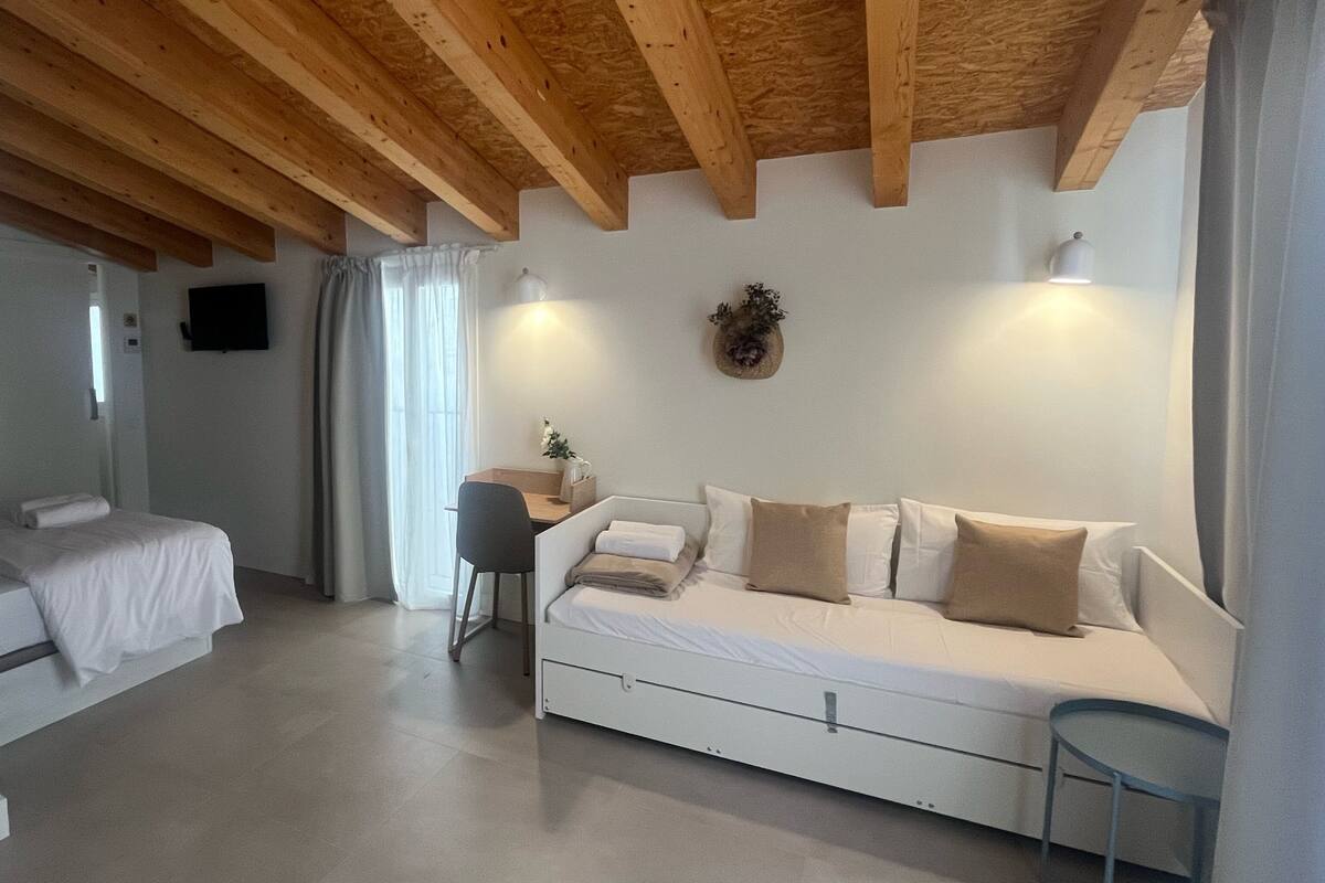 A bedroom with a bed, a desk, a chair, and a sofa.