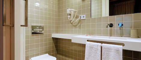 A bathroom with a toilet, a sink, a mirror, and two towels hanging on the wall.