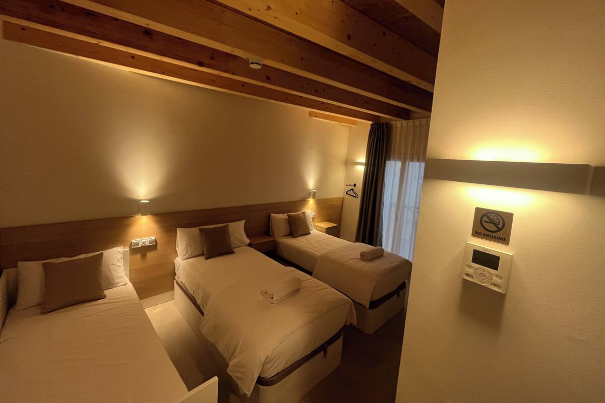 A hotel room with two beds, a wooden ceiling, a 'No Smoking' sign, and a thermostat on the wall.