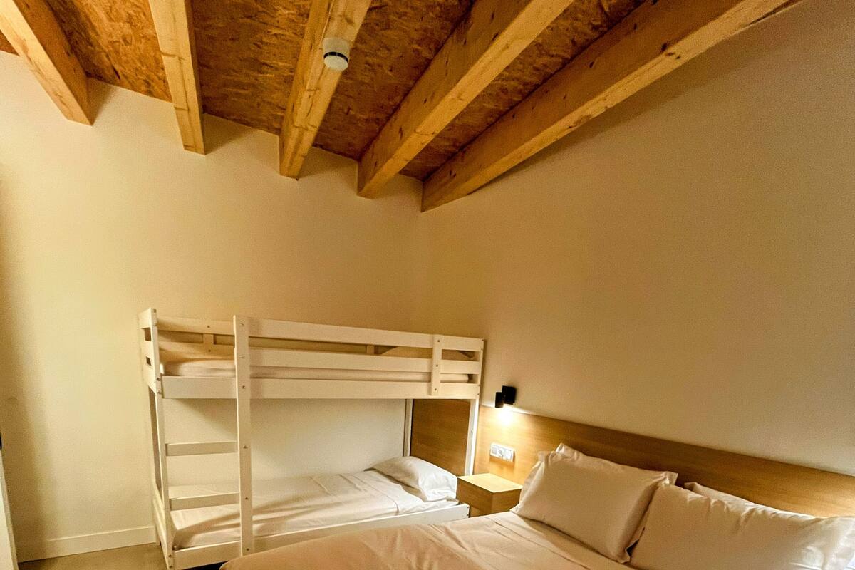 A room with a bunk bed, a single bed, and a nightstand with a lamp.