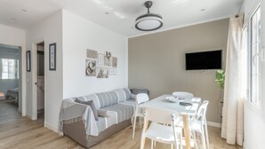 A modern living room with a sofa, dining table, chairs, a flat-screen TV, and a ceiling fan. - Holiday Apartment 'Giuliana' with Shared Pool, Wi-Fi, and Air Conditioning (San Jaime Mediterráneo)