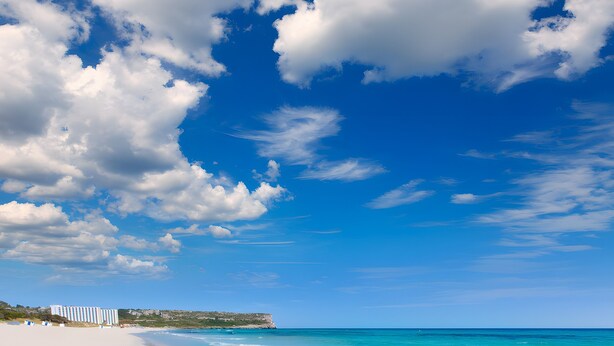 A beach with clear turquoise water, a sandy shore, and a building in the background. - Holiday Apartment 'Giuliana' with Shared Pool, Wi-Fi, and Air Conditioning (San Jaime Mediterráneo)