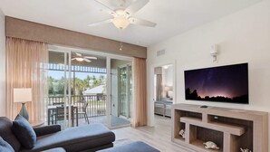 En moderne stue med et fladskærms-tv, grå sofaer, en loftventilator og en skydedør af glas, der fører til et udendørs område.