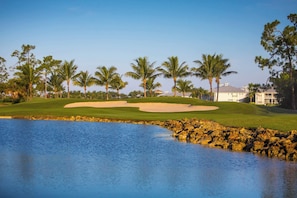 Ein Golfplatz mit Sandbunkern, einem Wasserlauf und Palmen.