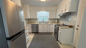 A kitchen with white cabinets, a stainless steel refrigerator, a dishwasher, and a window with blinds. - Masters Week Rental-Spacious cottage in town! (Aiken)