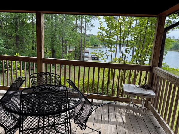 A wooden deck with a table and chairs, overlooking a lake and trees.