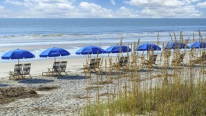 A beach with rows of blue umbrellas and beach chairs. - Palmetto Dunes Villa – Golf, Pools & Bike to Beach (Hilton Head Island)