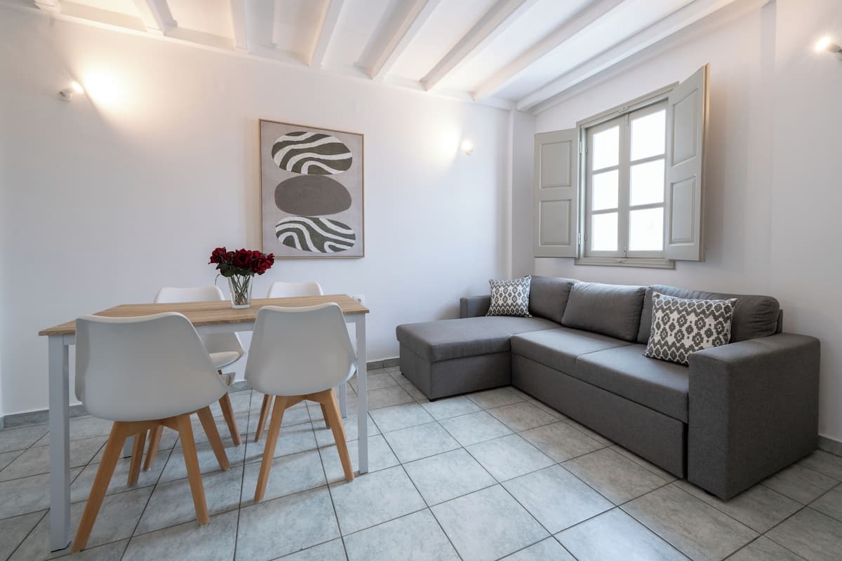 A modern living room with a gray sectional sofa, a dining table with chairs, a vase of red flowers, and a zebra print artwork on the wall.