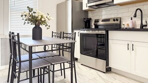 A modern kitchen with white cabinets, a built-in oven, a microwave, and a dining area with a table and chairs. - Fully Renovated 2BR Executive Residence Near NYC (Cliffside Park)