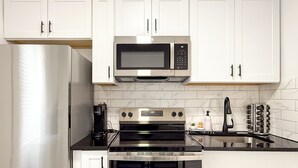 A modern kitchen with white cabinets, a stainless steel refrigerator, a microwave, a stove, and a coffee maker. - Fully Renovated 2BR Executive Residence Near NYC (Cliffside Park)