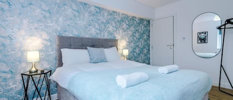 Un dormitorio con una cama, dos lámparas de noche, un espejo en la pared y un cartel que indica 'A-K Apartments'.