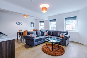Een moderne woonkamer met een hoekbank, een glazen salontafel en een eethoek met een tafel en stoelen.