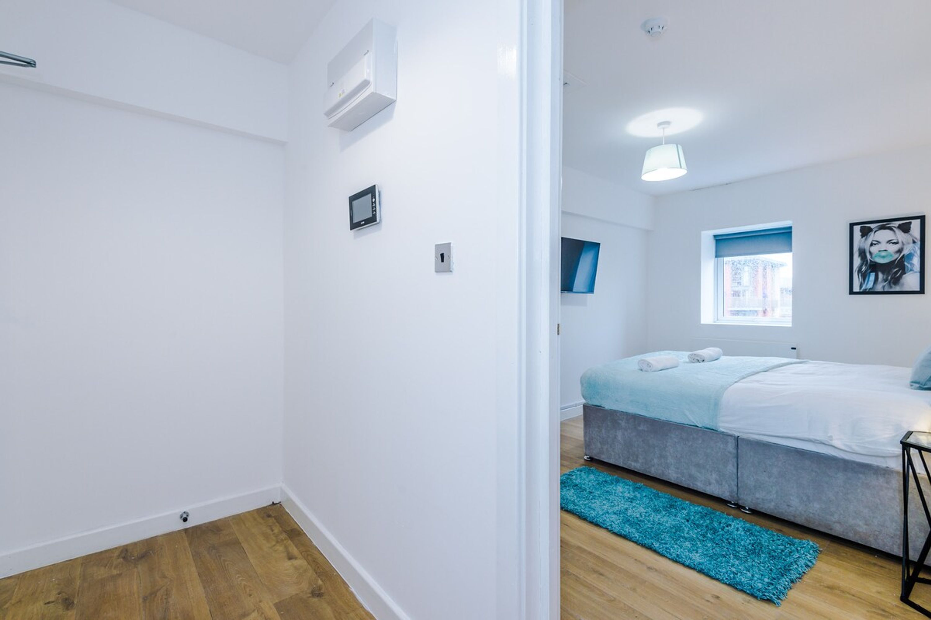 A modern bedroom with a bed, a small bedside table, a window with a view, and a blue rug.