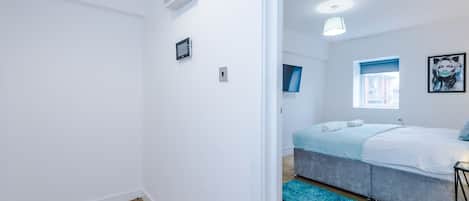 A modern bedroom with a bed, a small bedside table, a window with a view, and a blue rug.
