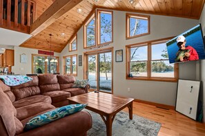 A spacious living room with a brown leather couch, wooden coffee table, and large windows offering views of the outdoors. - LakeFront Manitowish Waters Cabin + Loft (Manitowish Waters)