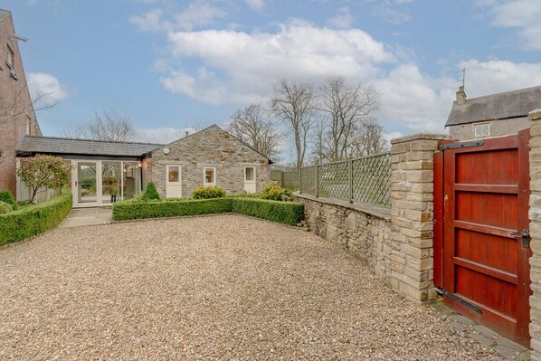 A stone building with a gravel driveway, a wooden fence, and a red gate.