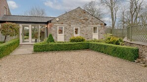 A stone house with a gravel driveway, a glass door entrance, and a well-maintained hedge.