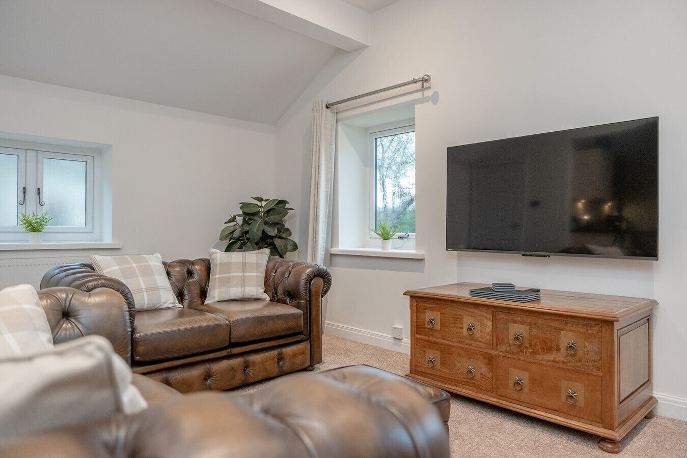Una sala de estar con sofá de cuero, cómoda de madera, televisor de pantalla plana y ventana con cortinas.