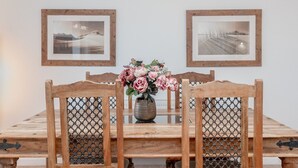 A dining table with chairs, a vase of flowers, and two framed pictures on the wall.