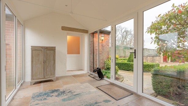 A spacious hallway with large windows, a wooden cabinet, and a rug.