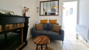 Een woonkamer met een open haard, een bank, een ronde houten tafel en een spiegel aan de muur.
