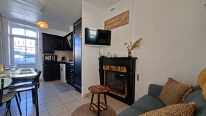 Een moderne keuken met donkere kastjes, een eethoek met een tafel en stoelen, een open haard en een flatscreen televisie aan de muur.