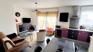 Un espacio habitable compacto con sofá, sillón, mesa de comedor, kitchenette y televisor.