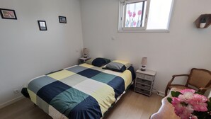Un dormitorio con cama, mesitas de noche, una silla, ventana con vistas y estante en la pared.