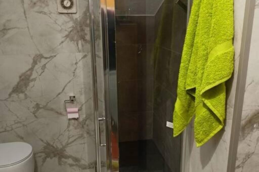 Een badkamer met een douchecabine van glas, een toilet en een handdoekrek met een handdoek.