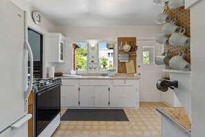 A compact kitchen with white cabinets, a stove, a sink, and a pegboard with mugs.