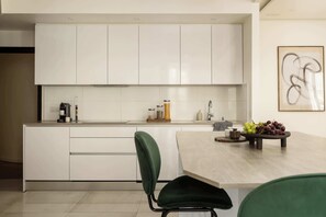 A modern kitchen with white cabinets, a dining table with chairs, and a fruit bowl on the table. - Champs Elysees Fancy Home 2BDR 6PPL (Paris)
