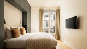 Ein modernes Schlafzimmer mit Bett, einem an der Wand montierten Fernseher und einem Fenster mit Vorhängen.