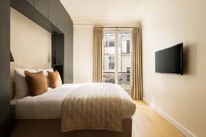 A modern bedroom with a bed, a TV mounted on the wall, and a window with curtains. - Classy Montaigne 2BR Suite 7P (Paris)