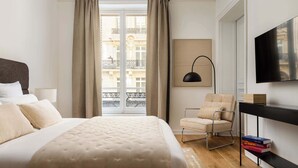 Una camera d'albergo con un letto, una sedia, una scrivania, una televisione e una finestra con tende.