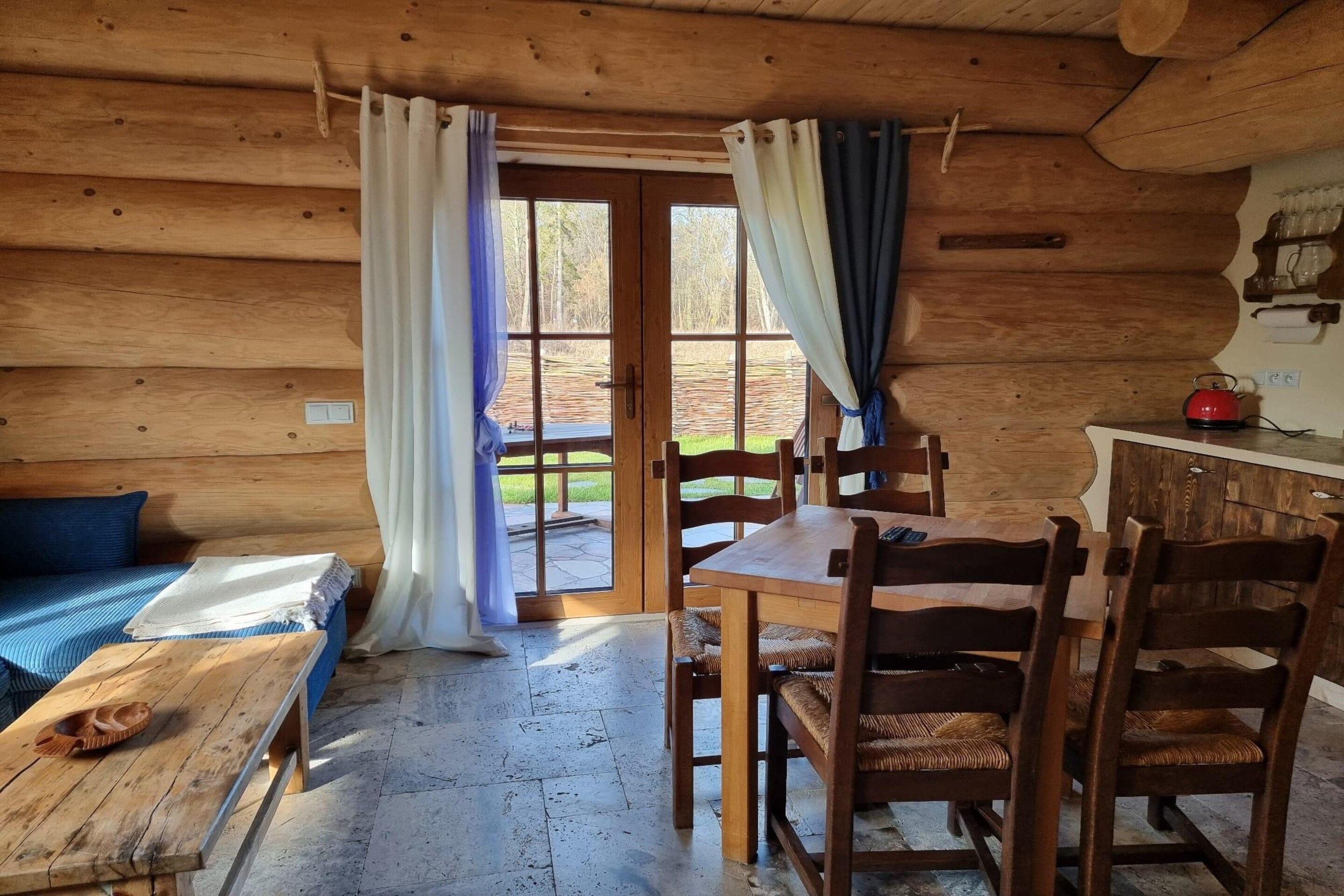 Ein Interieur einer Holzhütte mit einem Esstisch, Stühlen, einer Bank und einem kleinen Tisch mit einem Teekessel.