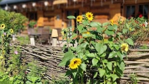 Una casa de madera con techo de paja, rodeada por un jardín lleno de girasoles.