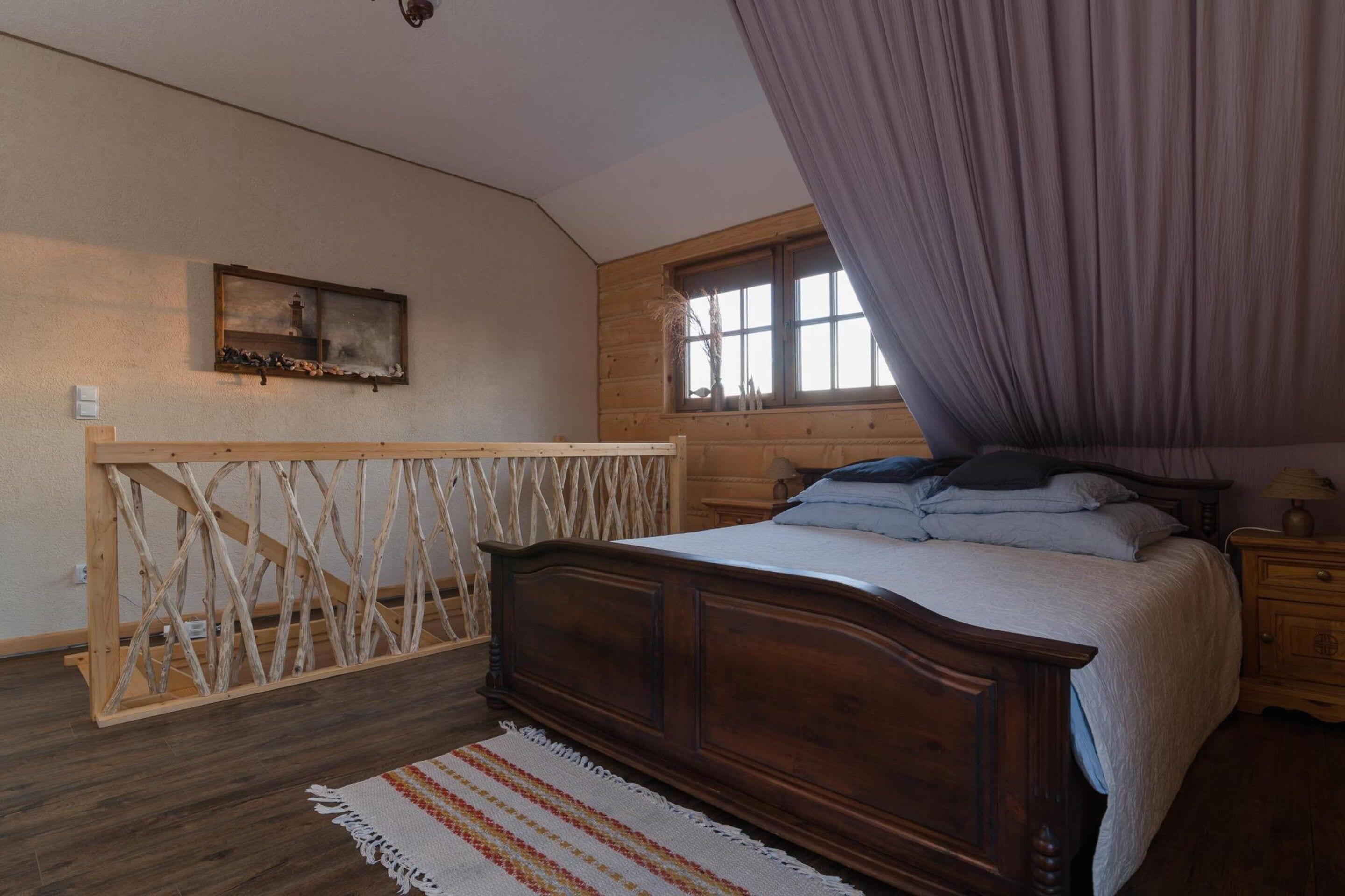 A bedroom with a wooden bed, a window with curtains, a wooden headboard, and a small bedside table.