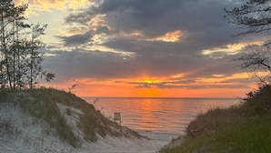 Escena de playa con atardecer, dunas de arena y una silla.