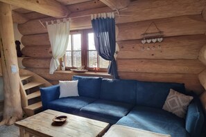 A log cabin interior with a blue sofa, a wooden table, and a window with curtains. - Two-level Apartment With a Large Terrace (gmina Będzino)