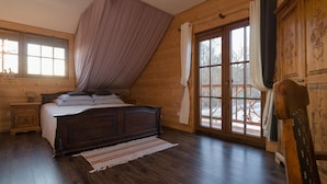 Una habitación con paneles de madera, una cama, una mesita de noche, una ventana con cortinas y vistas al exterior.