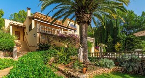 Une villa de style méditerranéen dotée d’un balcon, de palmiers et d’un jardin bien entretenu.