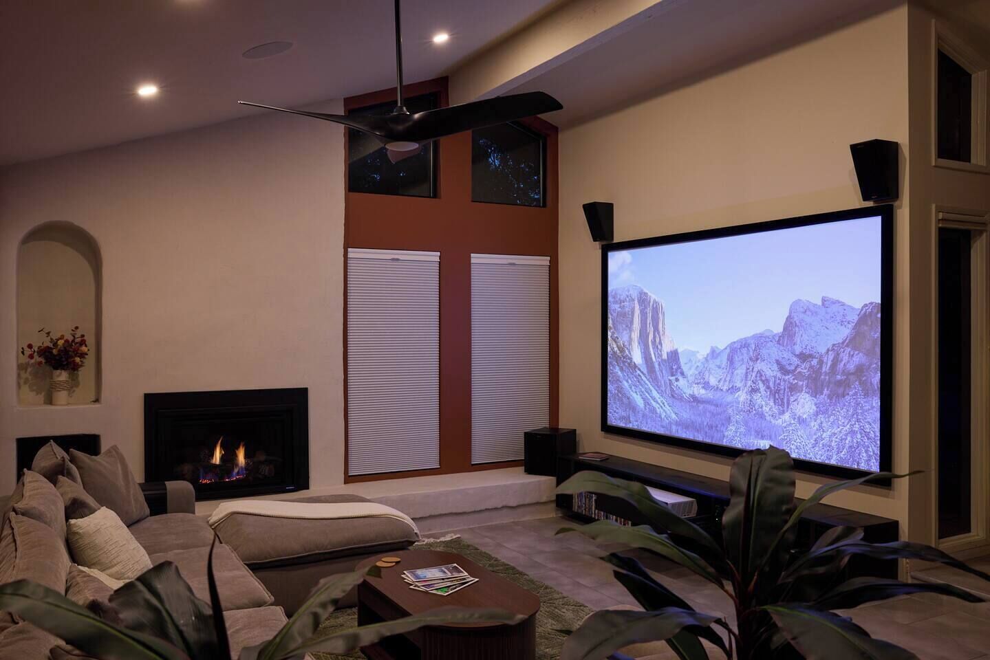 A living room with a fireplace, a large flat-screen TV, and a ceiling fan.