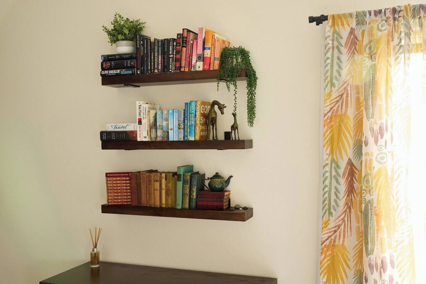 Drie houten planken met boeken, een kleine plant en een decoratief object.