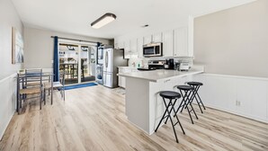 Una cocina moderna con armarios blancos, microondas, refrigerador y una barra con taburetes.