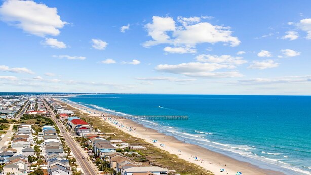 Un pueblo costero con playa, muelle y edificios residenciales a lo largo de la orilla.