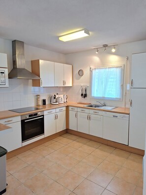 A modern kitchen with white cabinets, a built-in oven, a dishwasher, and a window with curtains. - Villa Océane with heated swimming pool. (Les Sables-d'Olonne)