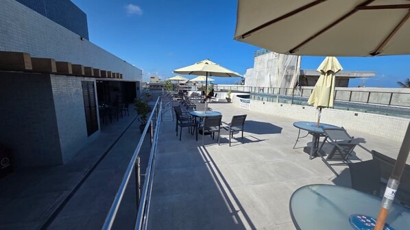 A rooftop terrace with outdoor seating, umbrellas, and a view of the ocean. - Ora Beach poucos passos do mar by LP (Ipojuca)