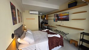 A hotel room with a bed, a TV, a kitchenette, and a dining area. - Ora Beach poucos passos do mar by LP (Ipojuca)